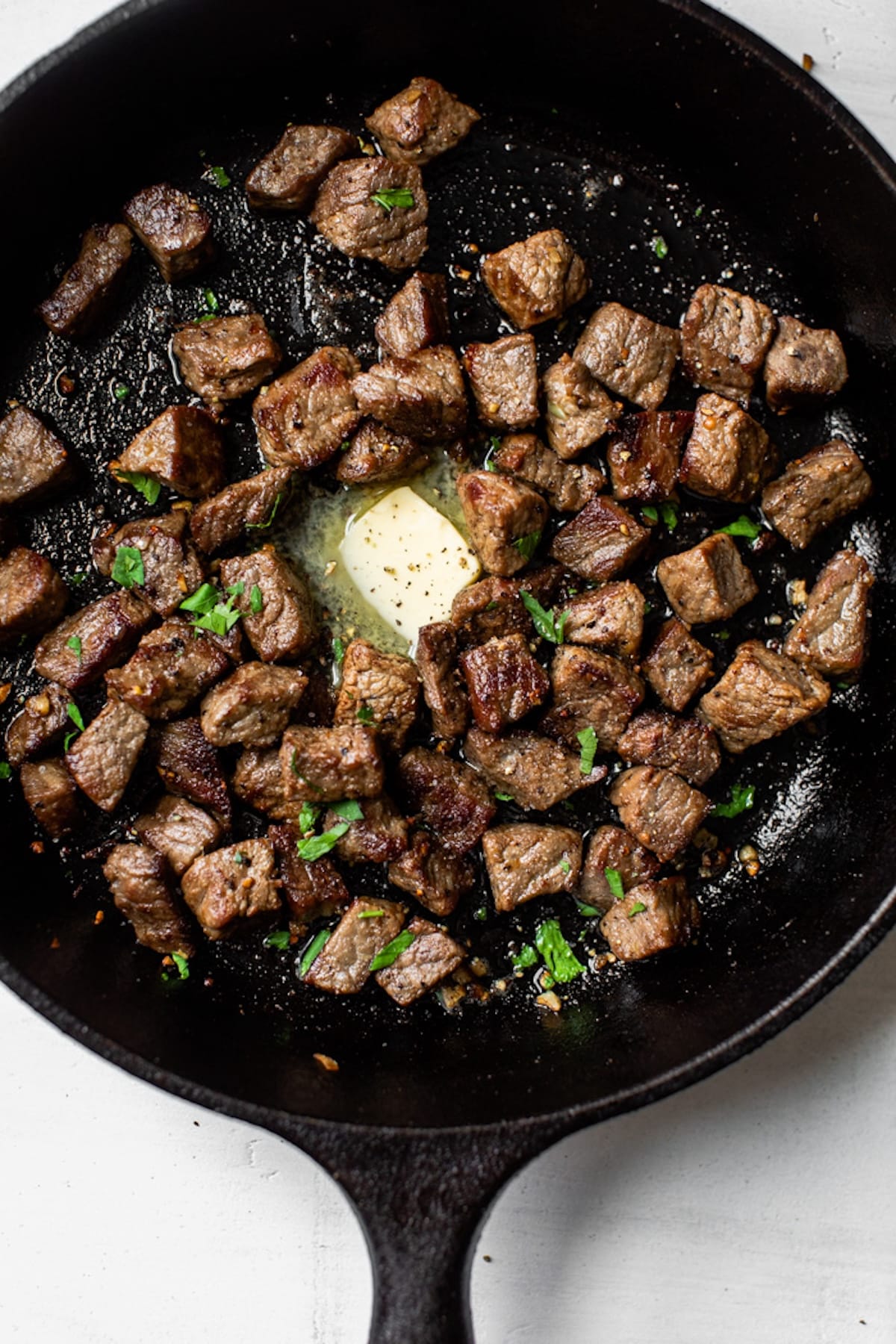 bite-sized steak in a cast iron skillet with butter and chopped parsley