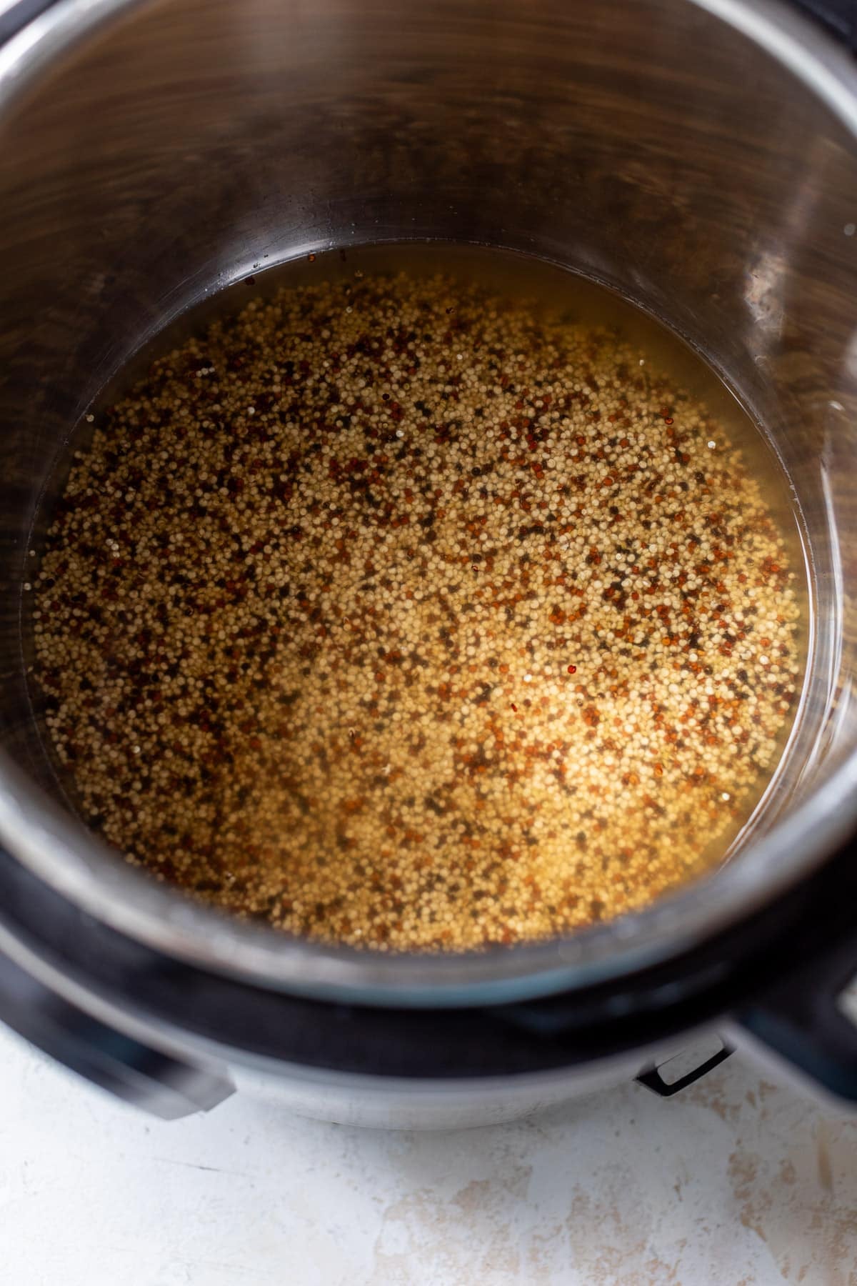 overhead view of uncooked quinoa and broth in an Instant Pot.