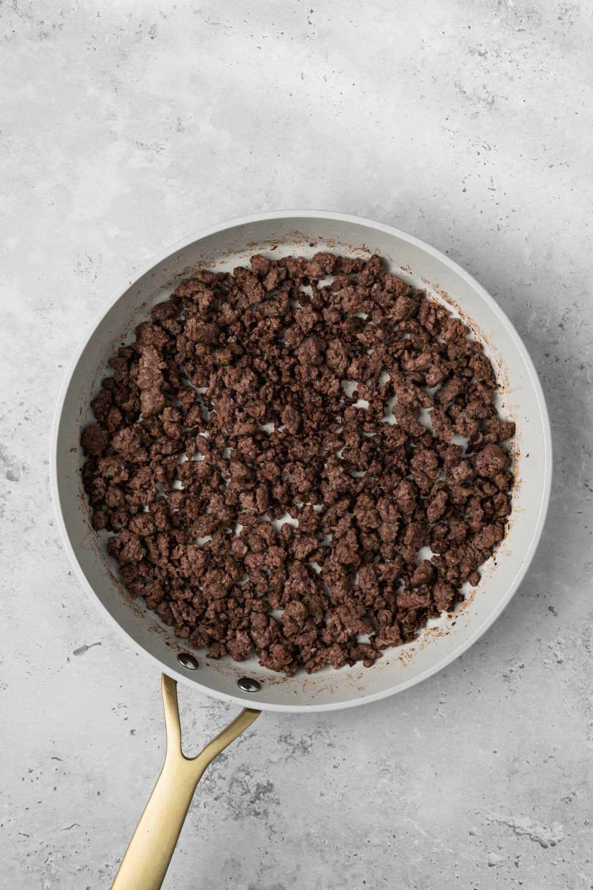 overhead view of cooked ground meat for breakfast burritos in a skillet.