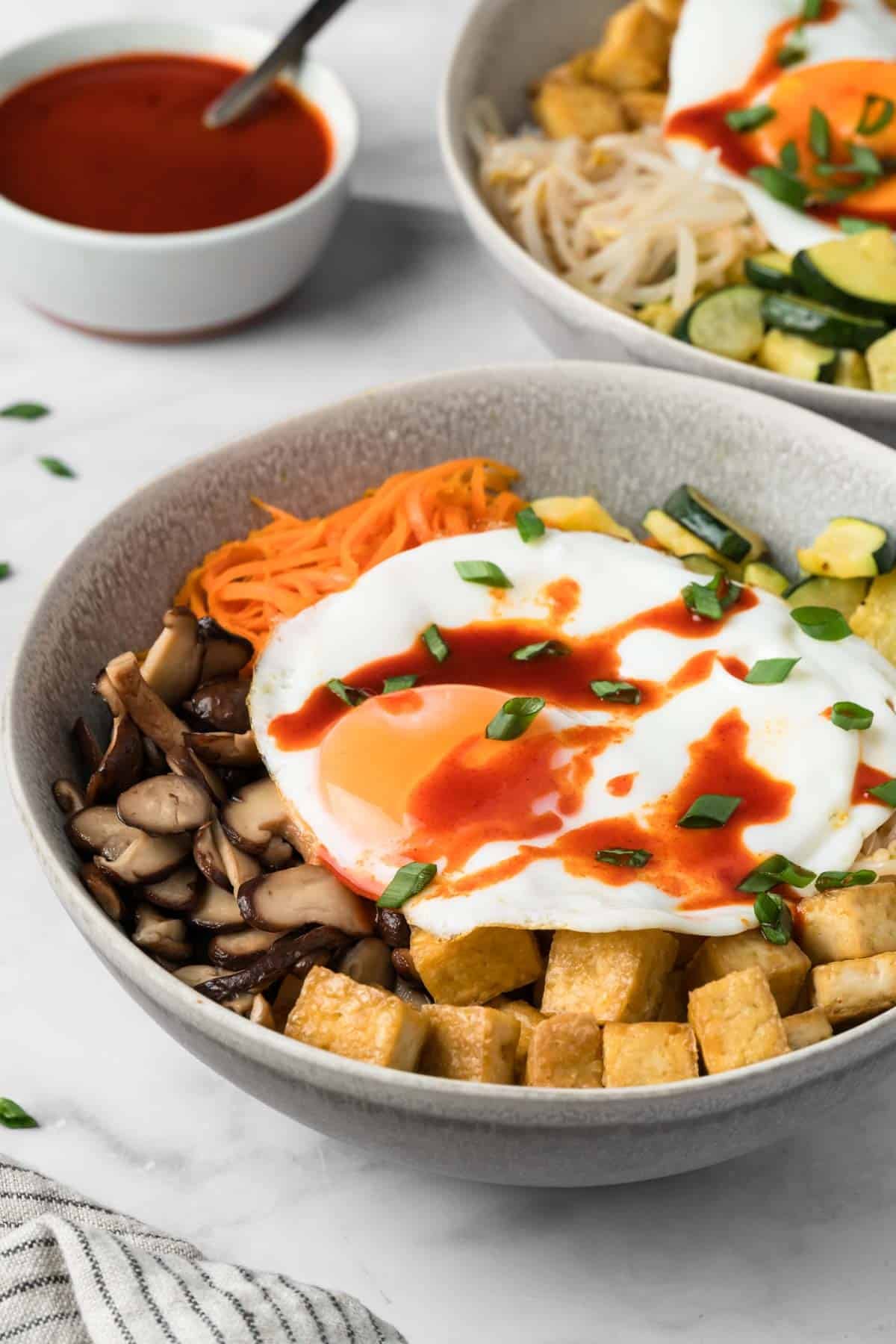 side view of tofu bibimbap topped with a fried egg in a bowl.