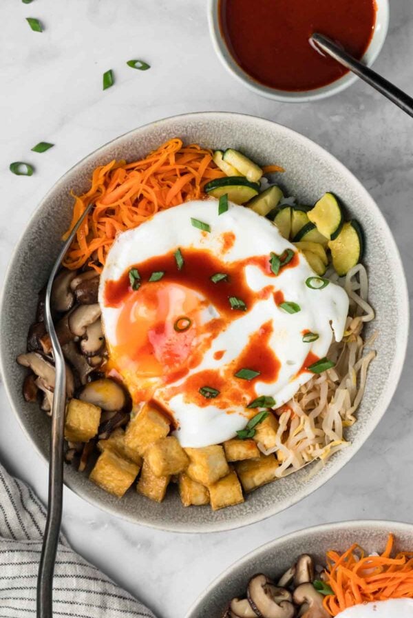 overhead view of tofu bibimbap topped with a fried egg in a bowl.
