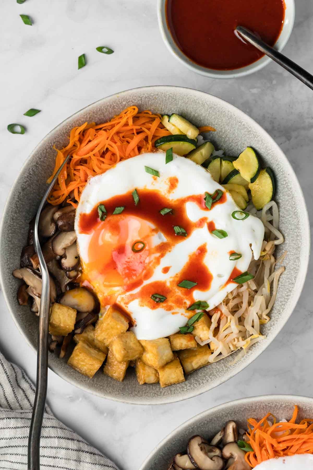 overhead view of tofu bibimbap topped with a fried egg in a bowl.
