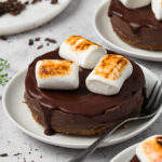 side view of 3 vegan s'mores cheesecakes on white plates with vegan marshmallows on top.
