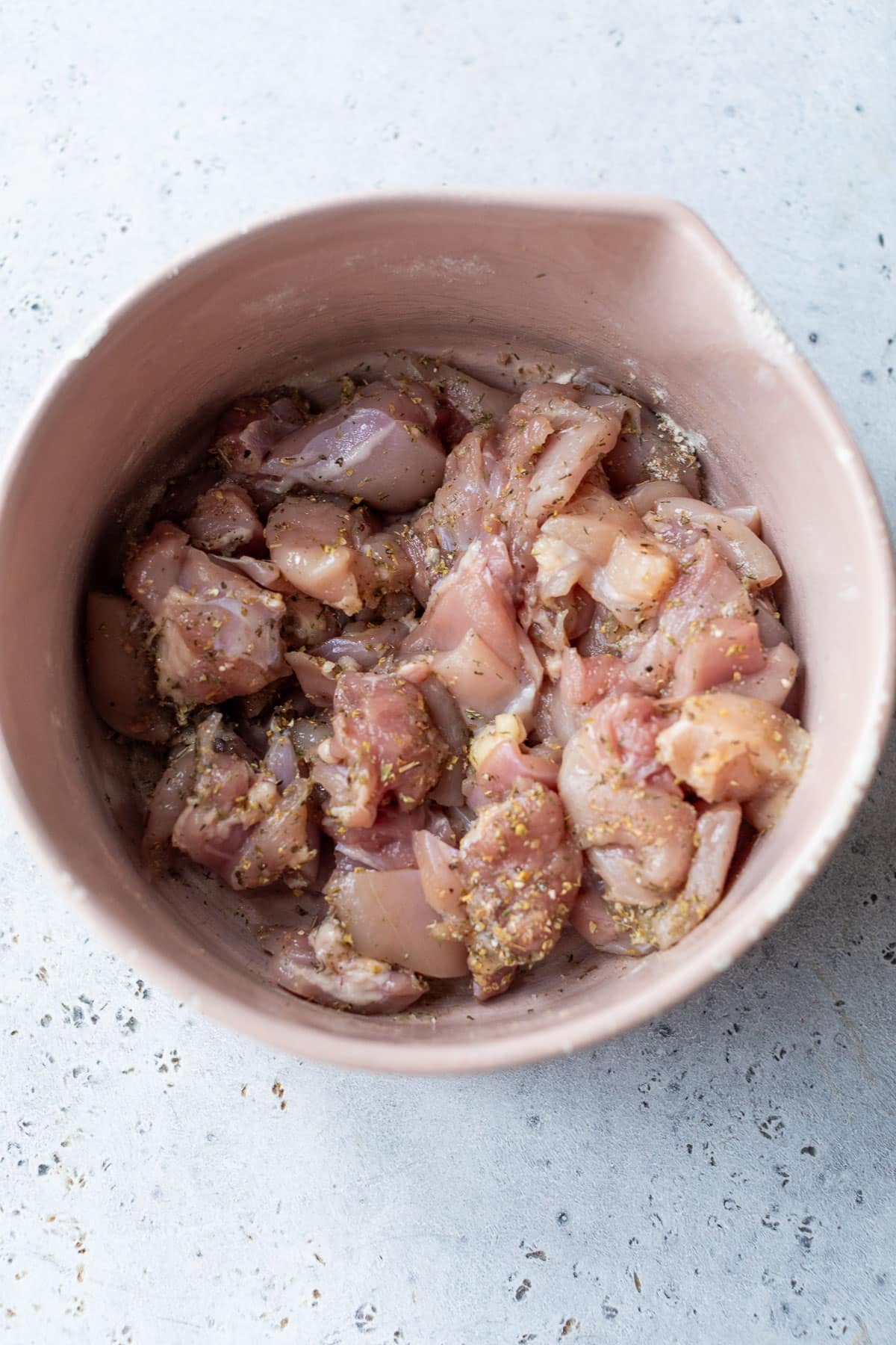 overhead view of raw chicken thigh pieces in a bowl with seasonings.