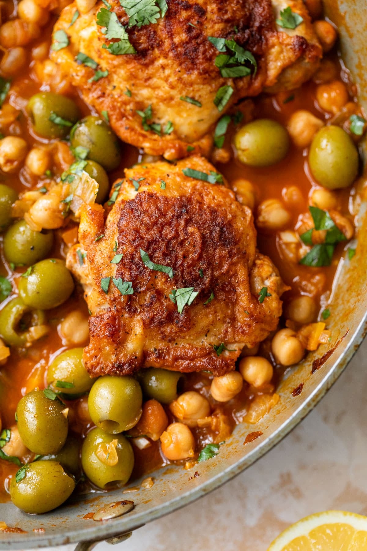 overhead view of Moroccan chicken thighs in a chickpea and olive sauce in a large pan.