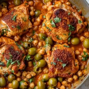 overhead view of Moroccan chicken thighs in a chickpea and olive sauce in a large pan.