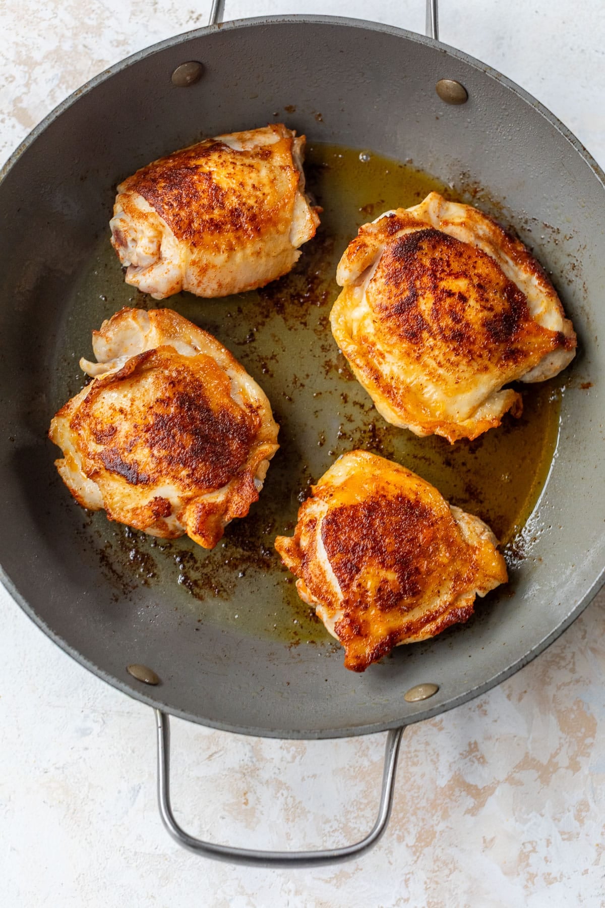 overhead view of seasoned chicken thighs being seared in a skillet.