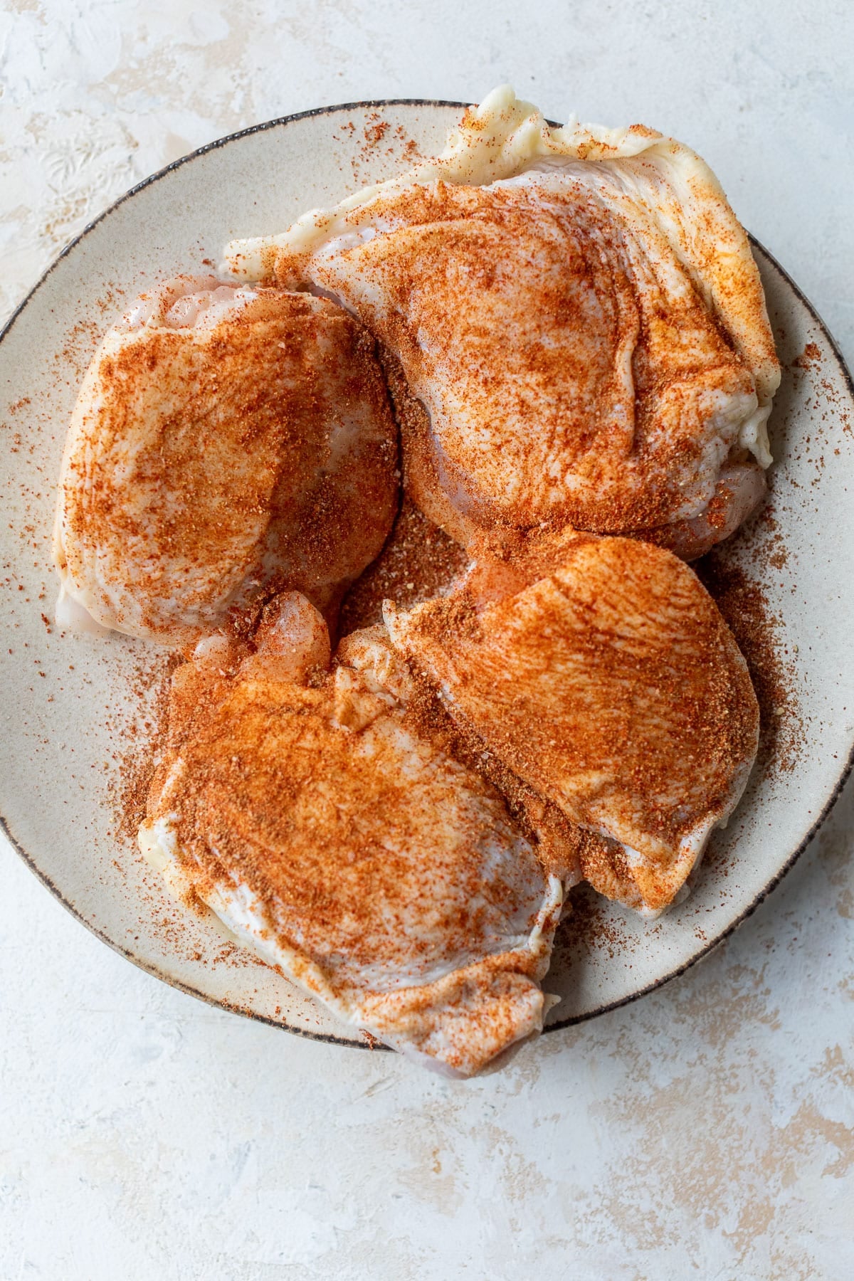 overhead view of seasoned chicken thighs on a plate.