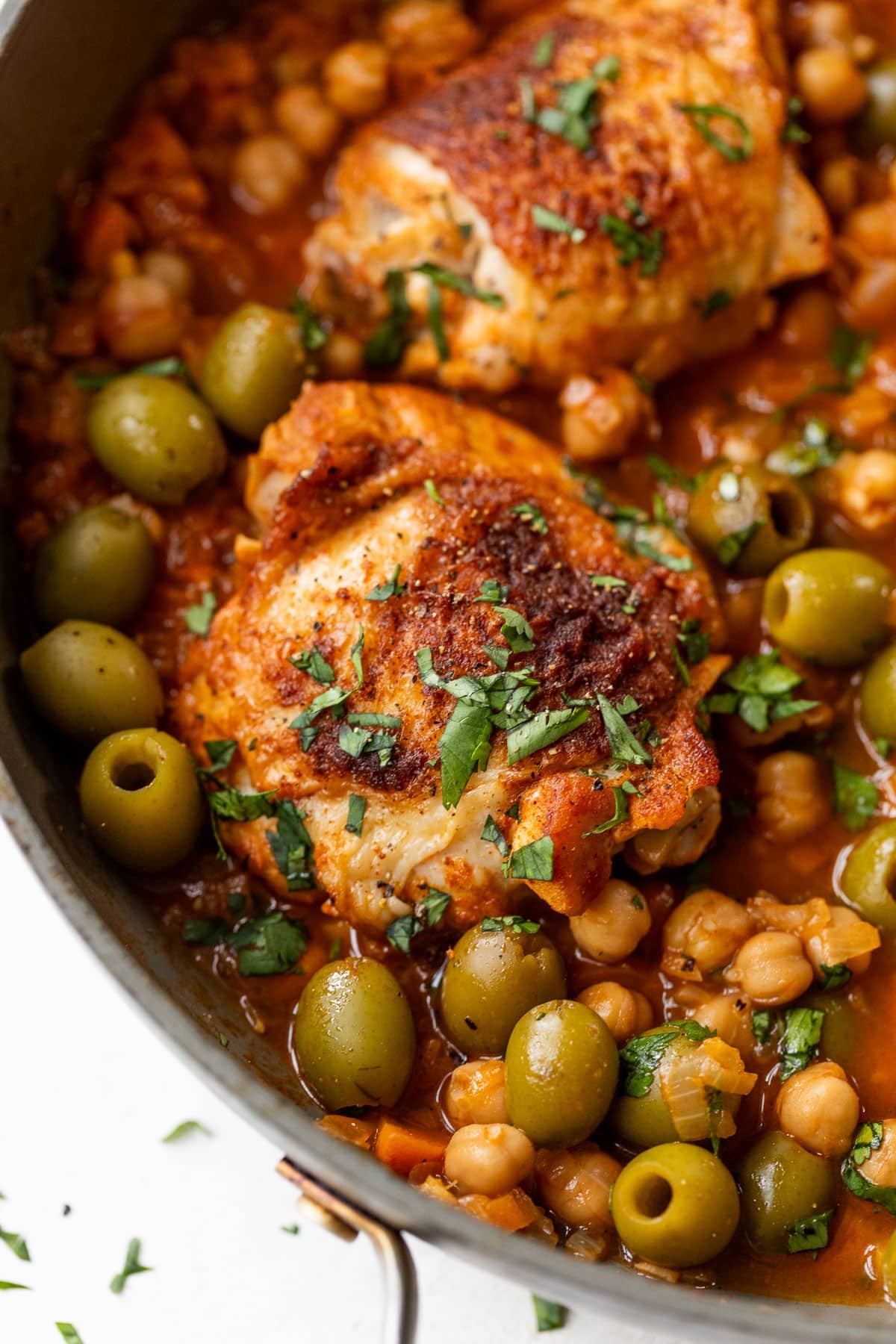 side view of Moroccan chicken thighs in a chickpea and olive sauce in a large pan.