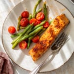 overhead view of a roasted salmon fillet on a plate with roasted green beans and tomatoes.