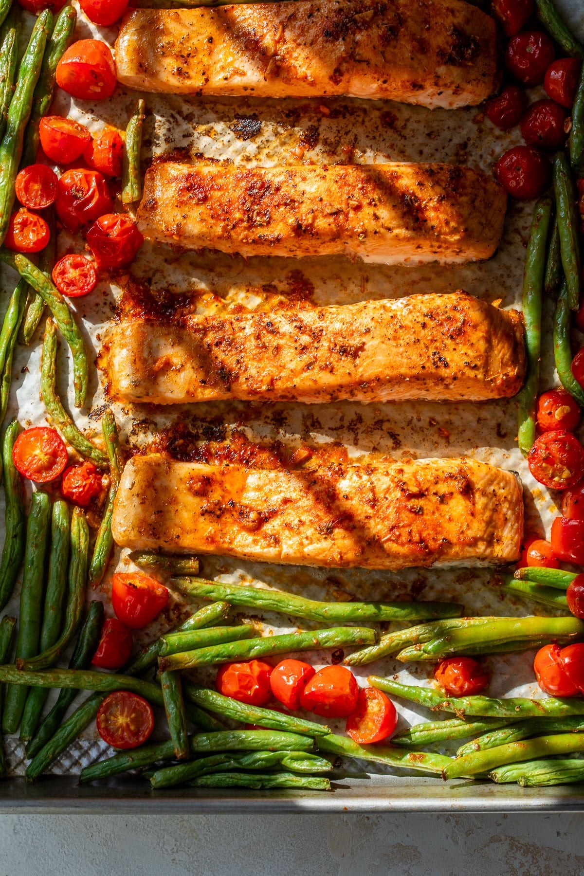 overhead view of roasted salmon fillets, green beans, and tomatoes on a sheet pan.