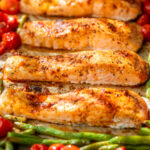 side view of roasted salmon fillets, green beans, and tomatoes on a sheet pan.
