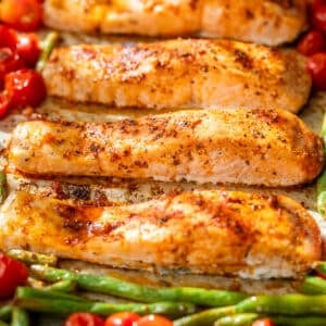 side view of roasted salmon fillets, green beans, and tomatoes on a sheet pan.