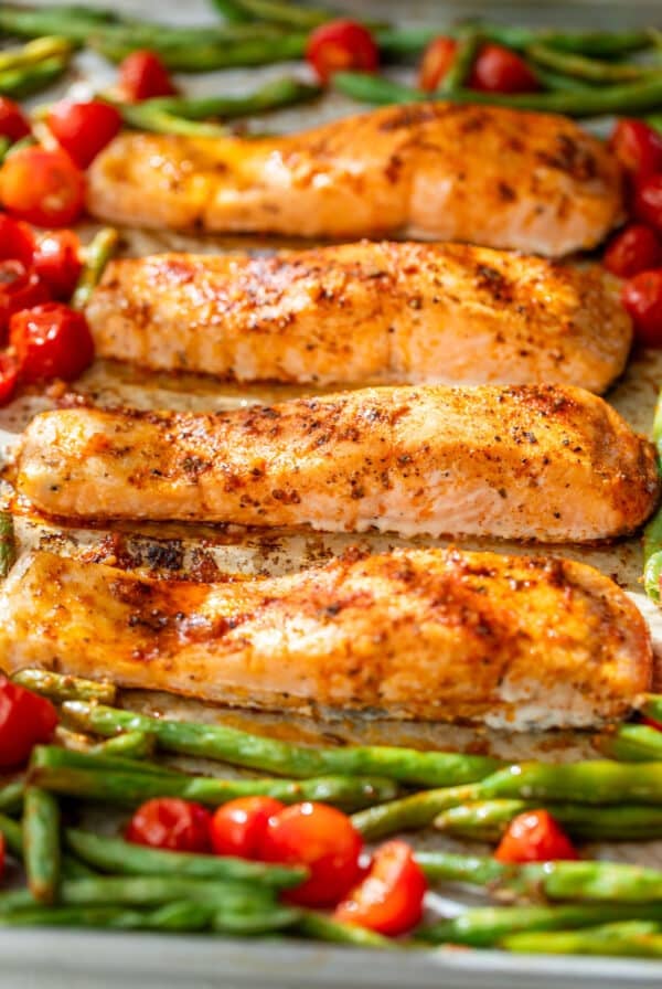 side view of roasted salmon fillets, green beans, and tomatoes on a sheet pan.