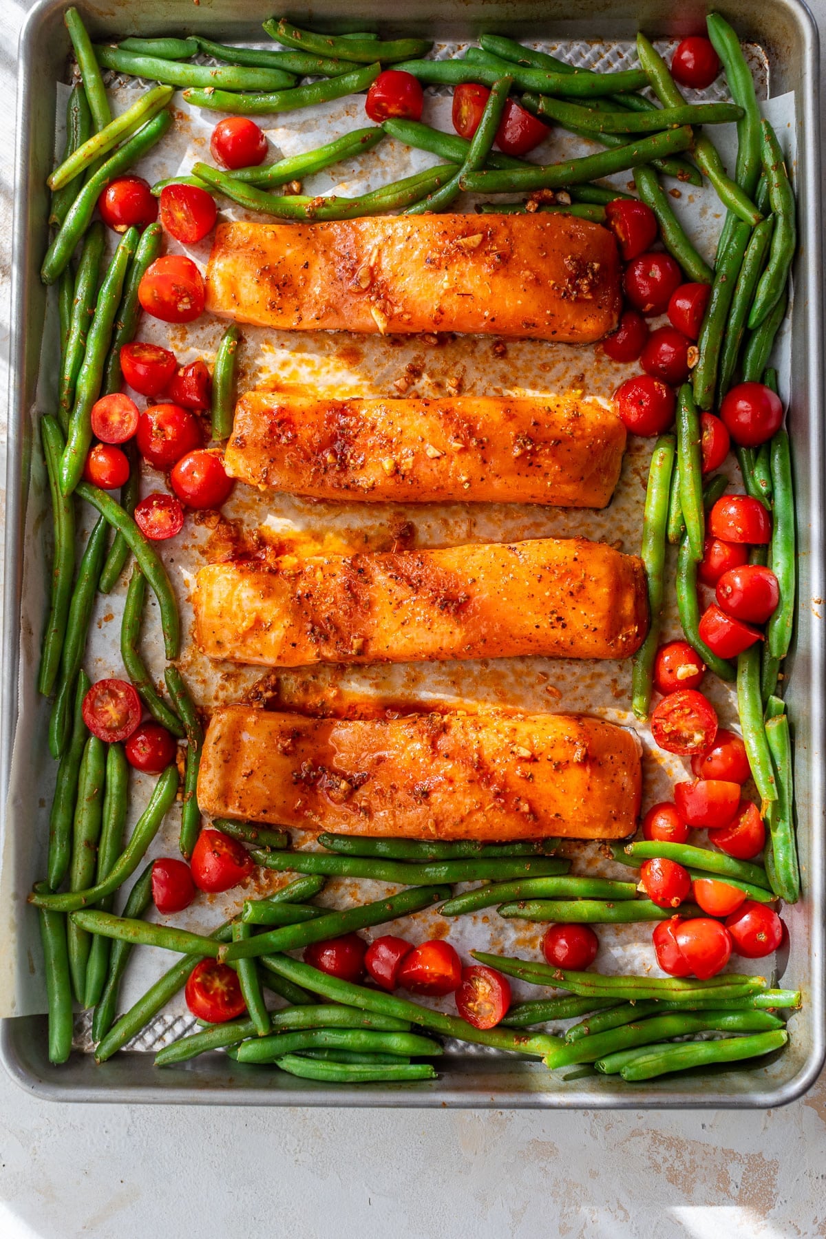 overhead view of raw salmon fillets, green beans, and tomatoes on a sheet pan.
