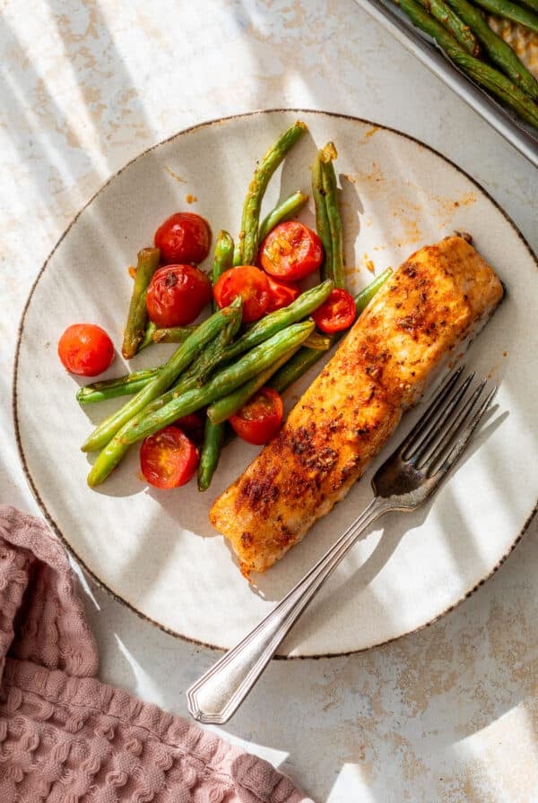 overhead view of a roasted salmon fillet on a plate with roasted green beans and tomatoes.