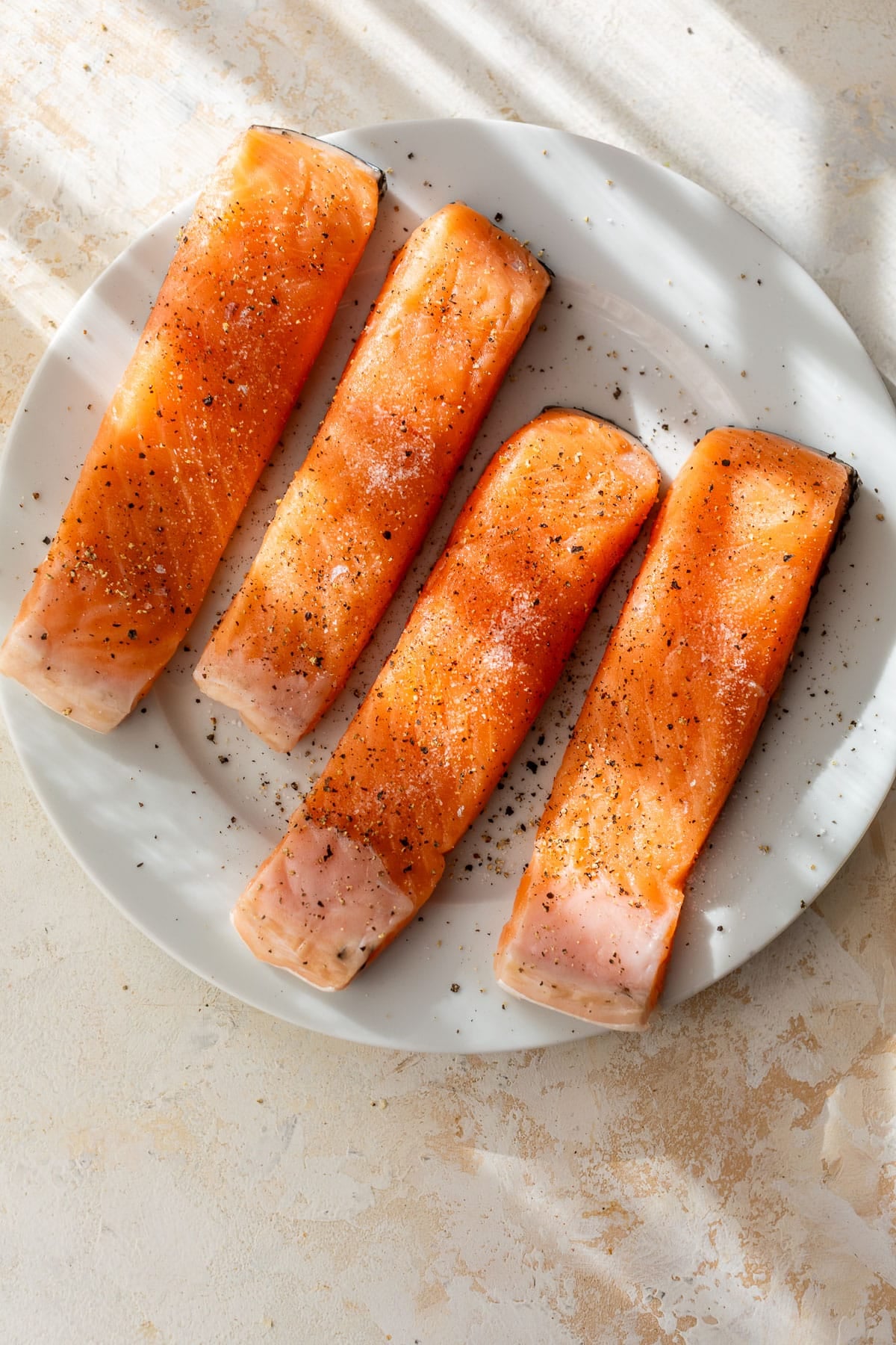 overhead view of 4 seasoned raw salmon fillets on a plate.