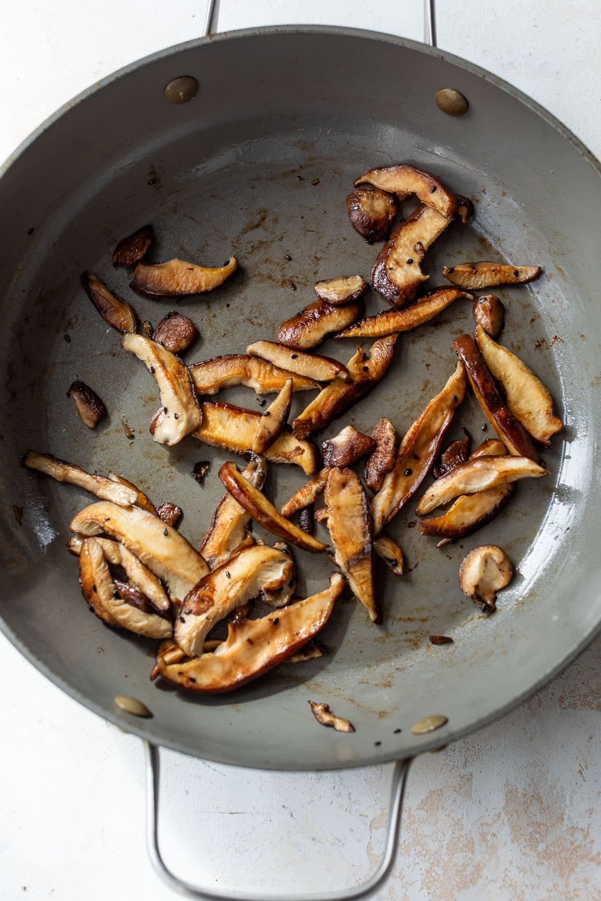 overhead view of shiitake mushrooms cooking in a skillet.