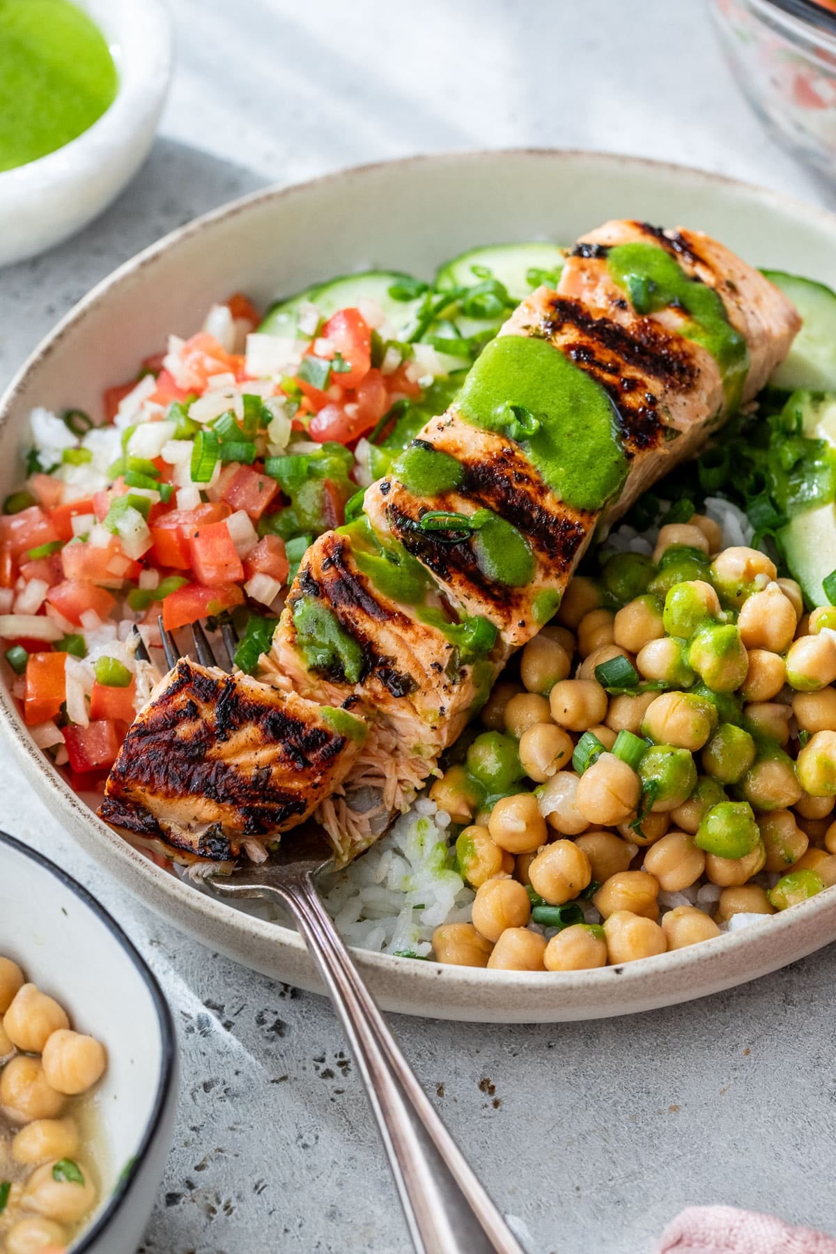 rice bowl topped with diced tomatoes, chickpeas and grilled salmon drizzled with a green dressing