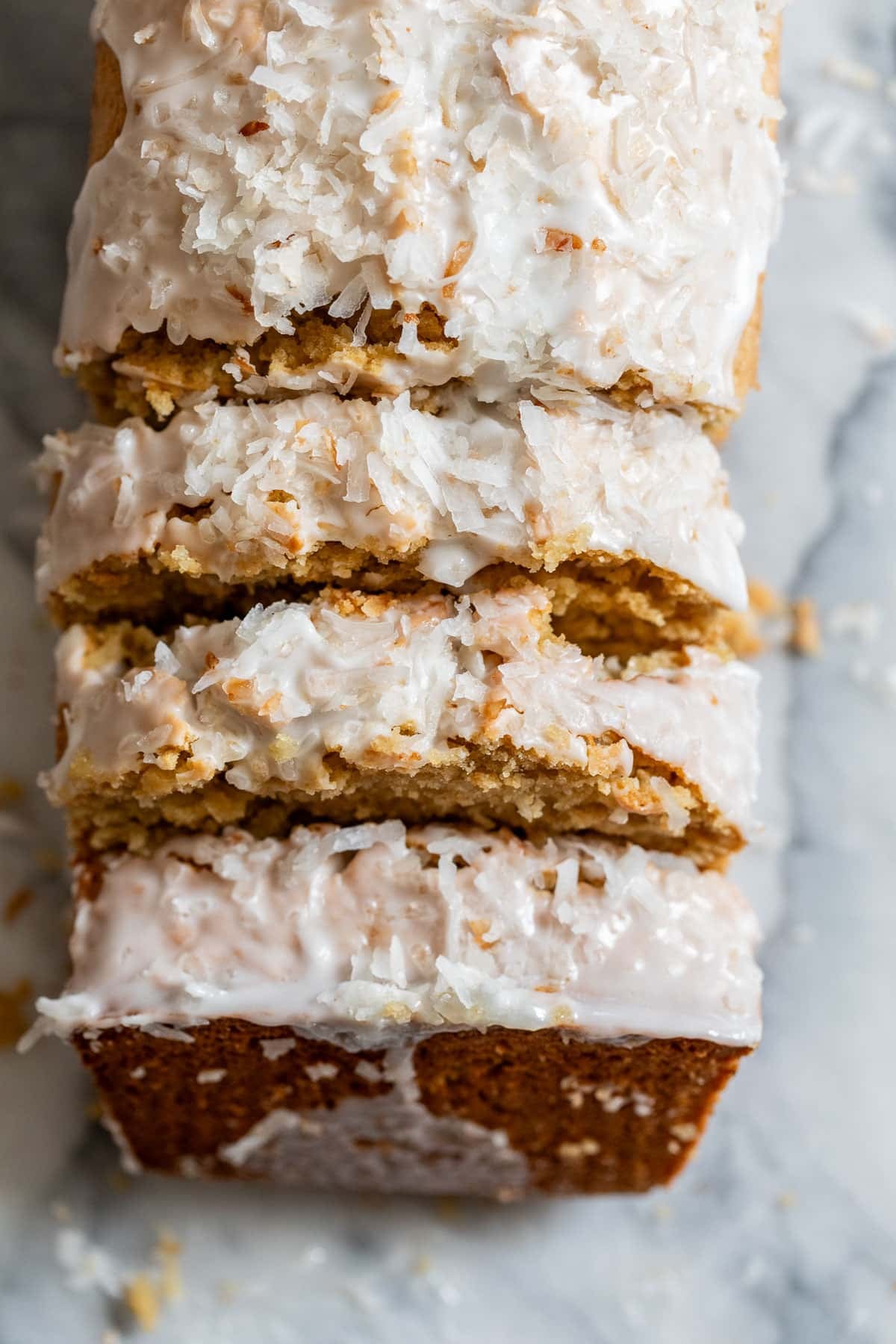 overhead view of a sliced and white glaze-topped loaf of sweet coconut bread.