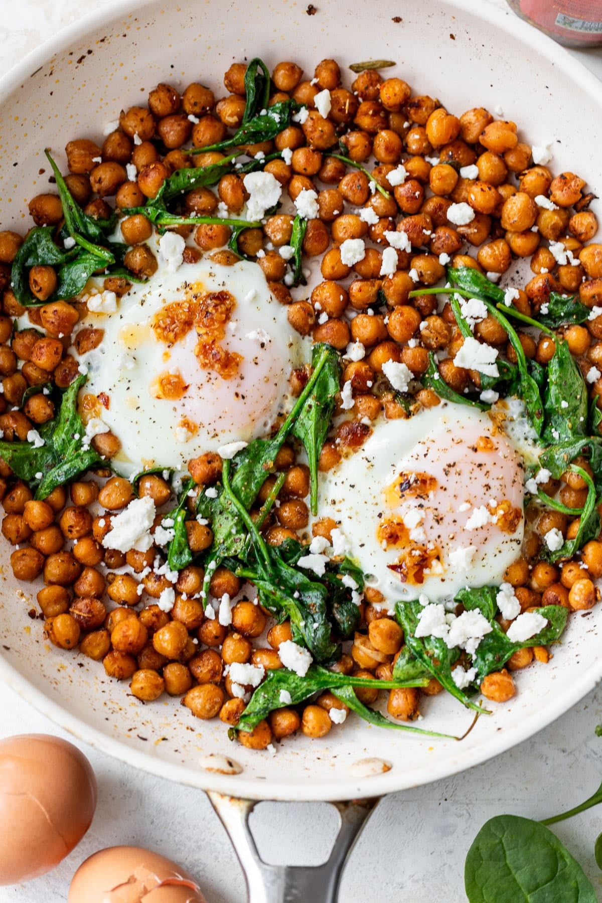 overhead view of cooked chickpeas, spinach, and 2 eggs topped with feta cheese in a skillet.