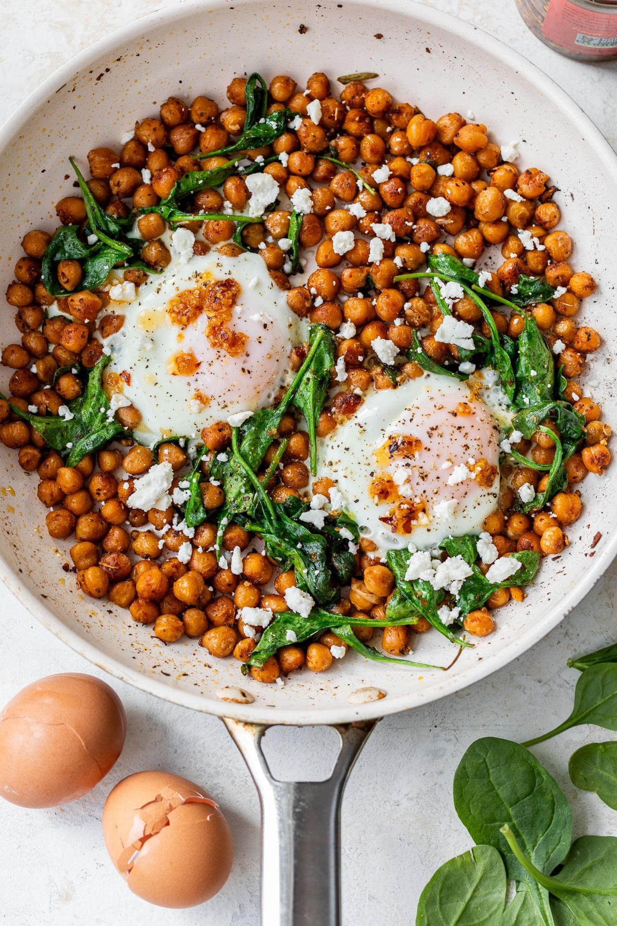 overhead view of cooked chickpeas, spinach, and 2 eggs topped with feta cheese in a skillet.