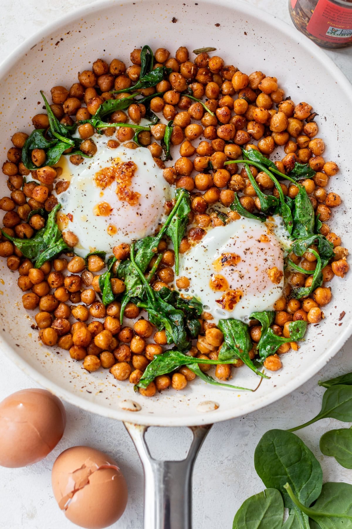 overhead view of cooked chickpeas, spinach, and 2 eggs in a skillet.