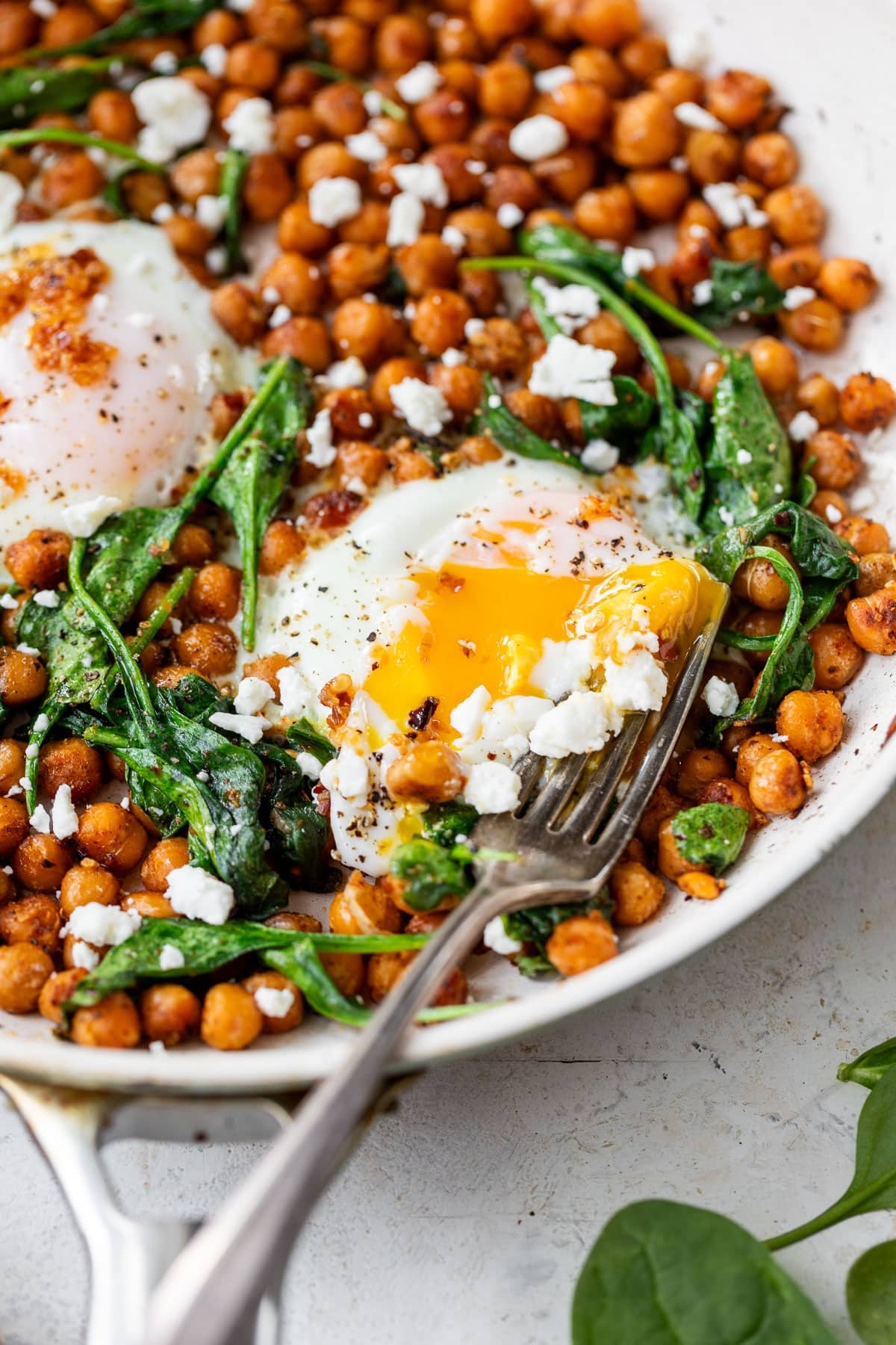 side view of a fork cutting into a cooked egg in an egg and chickpea breakfast skillet.