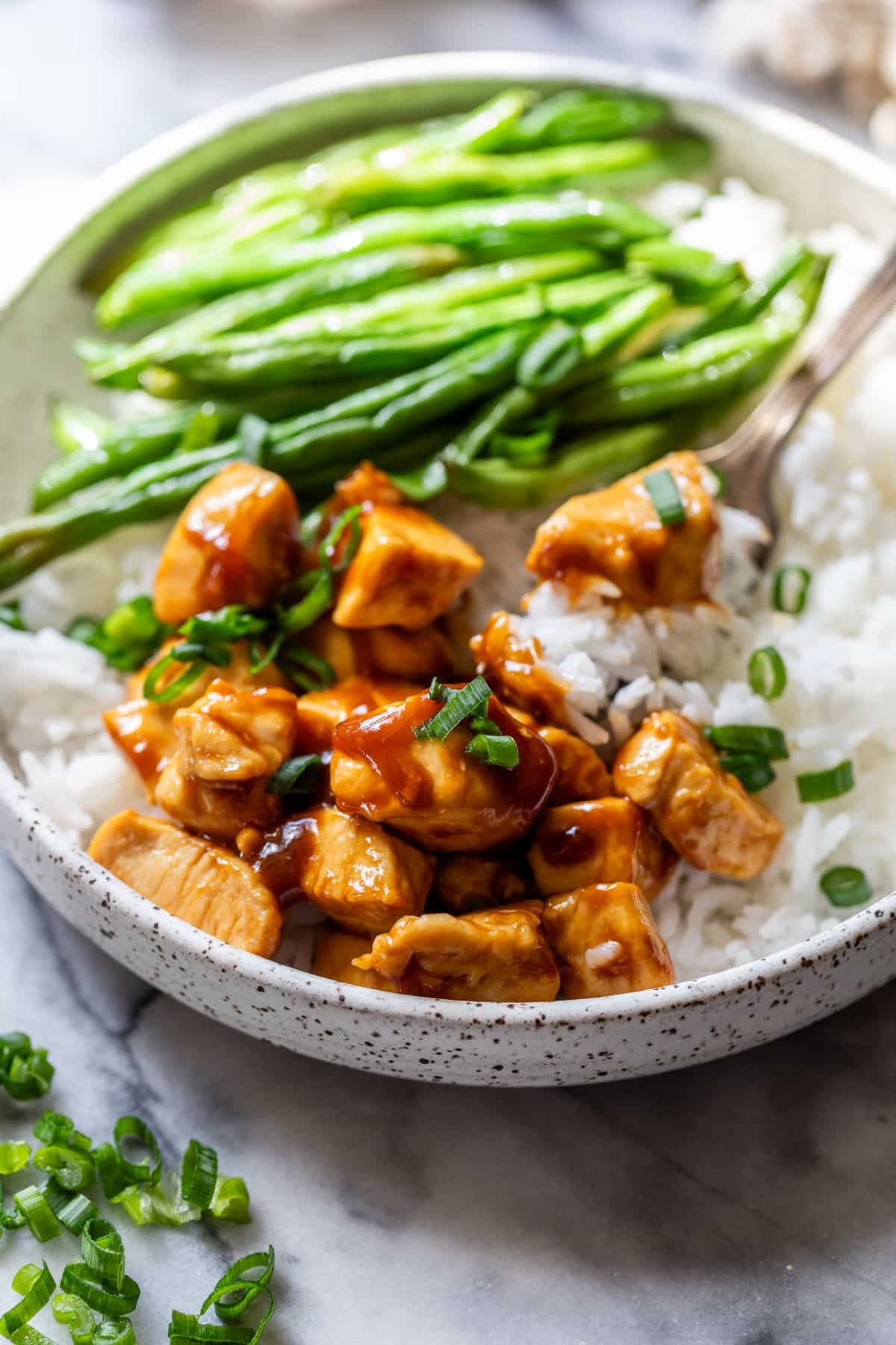 side view of healthy sesame chicken in a bowl with white rice and green beans.