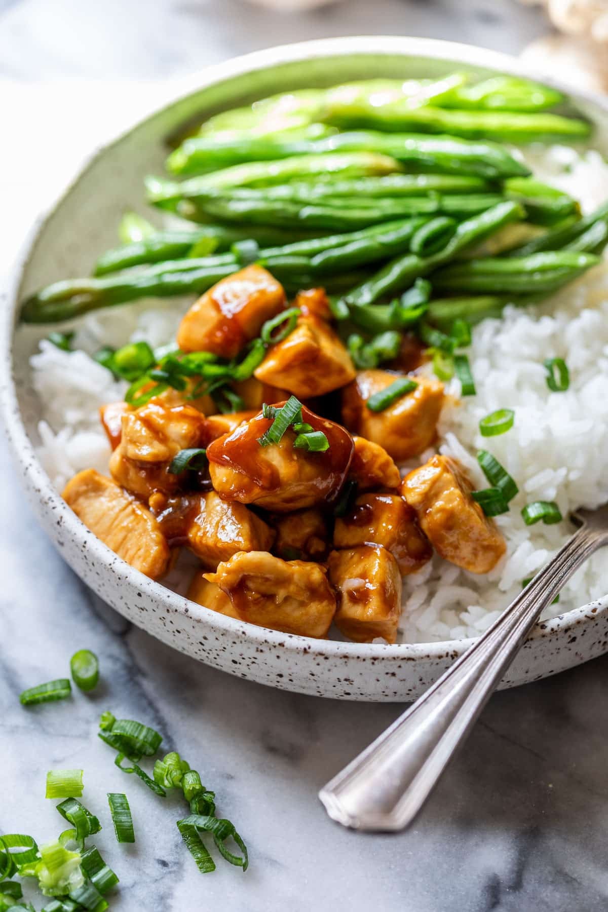 side view of healthy sesame chicken in a bowl with white rice and green beans.