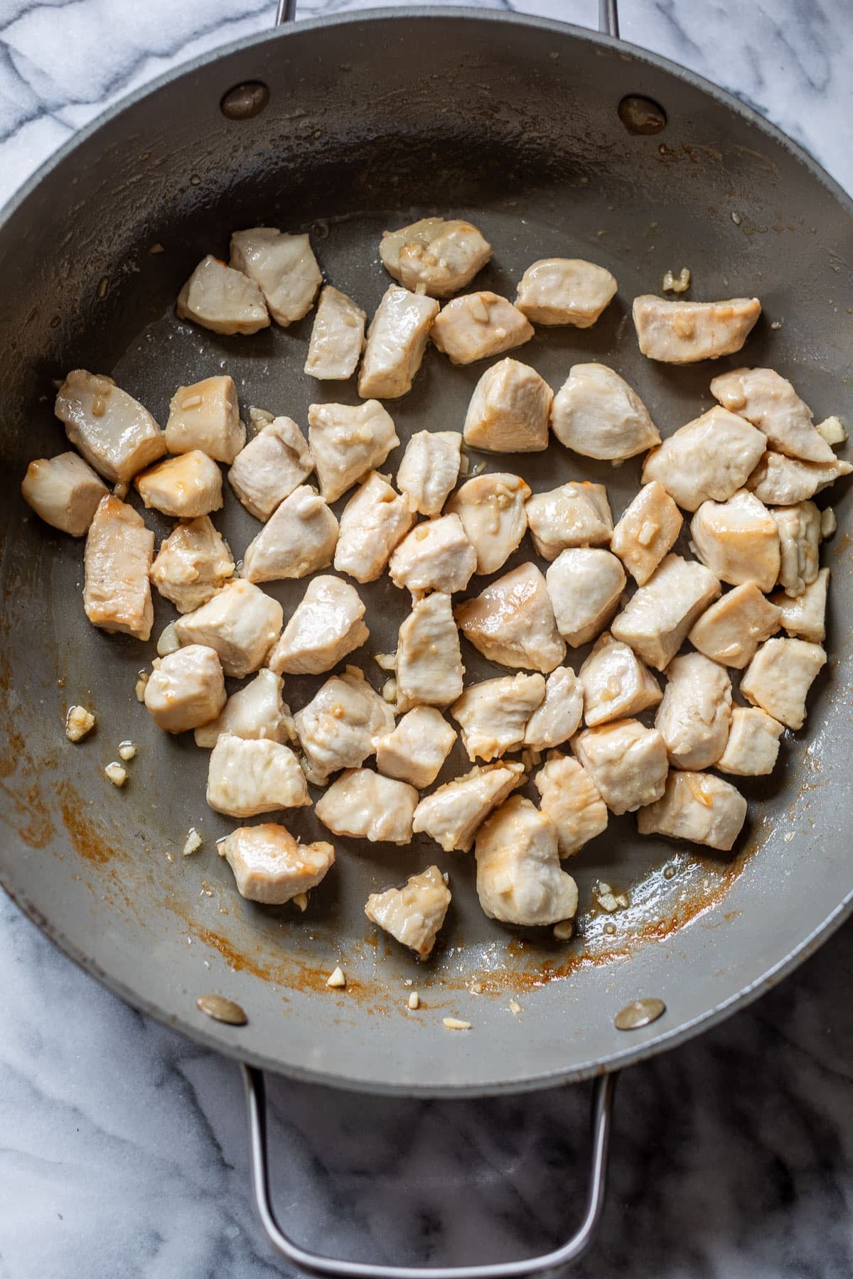 overhead view of chicken bites cooking in a large skillet.