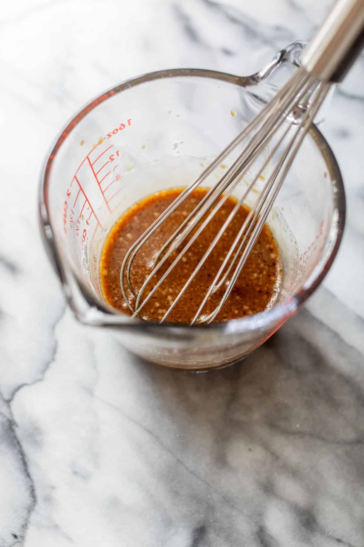 overhead view of sesame sauce and a whisk in a glass measuring cup.