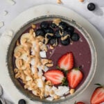 overhead view of a purple peanut butter acai bowl with fruit, peanut butter, and coconut on top.