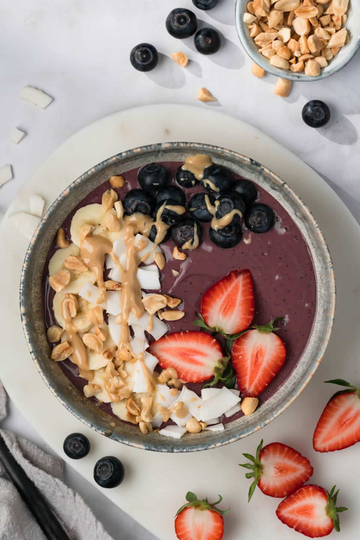 overhead view of a purple peanut butter acai bowl with fruit, peanut butter, and coconut on top.
