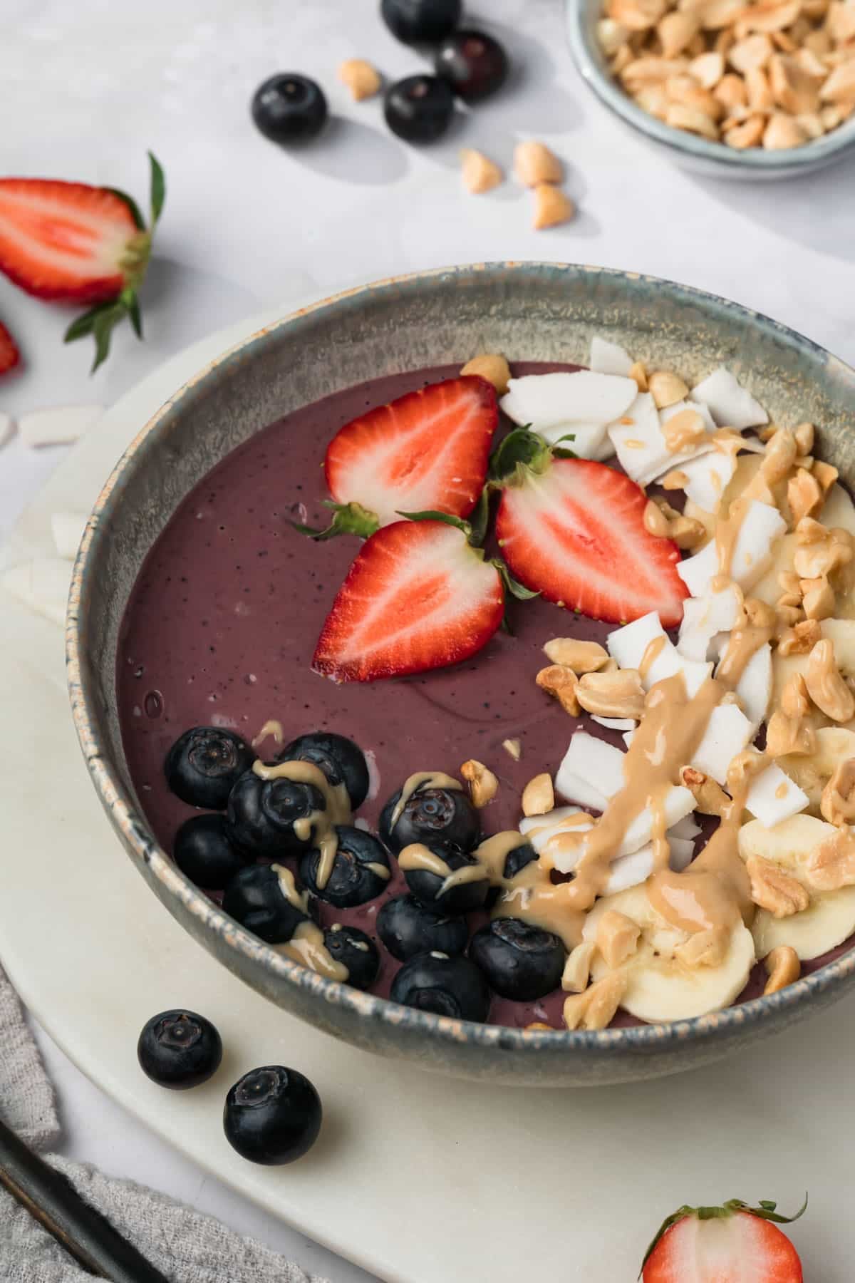 side view of a purple peanut butter acai bowl with fruit, peanut butter, and coconut on top.