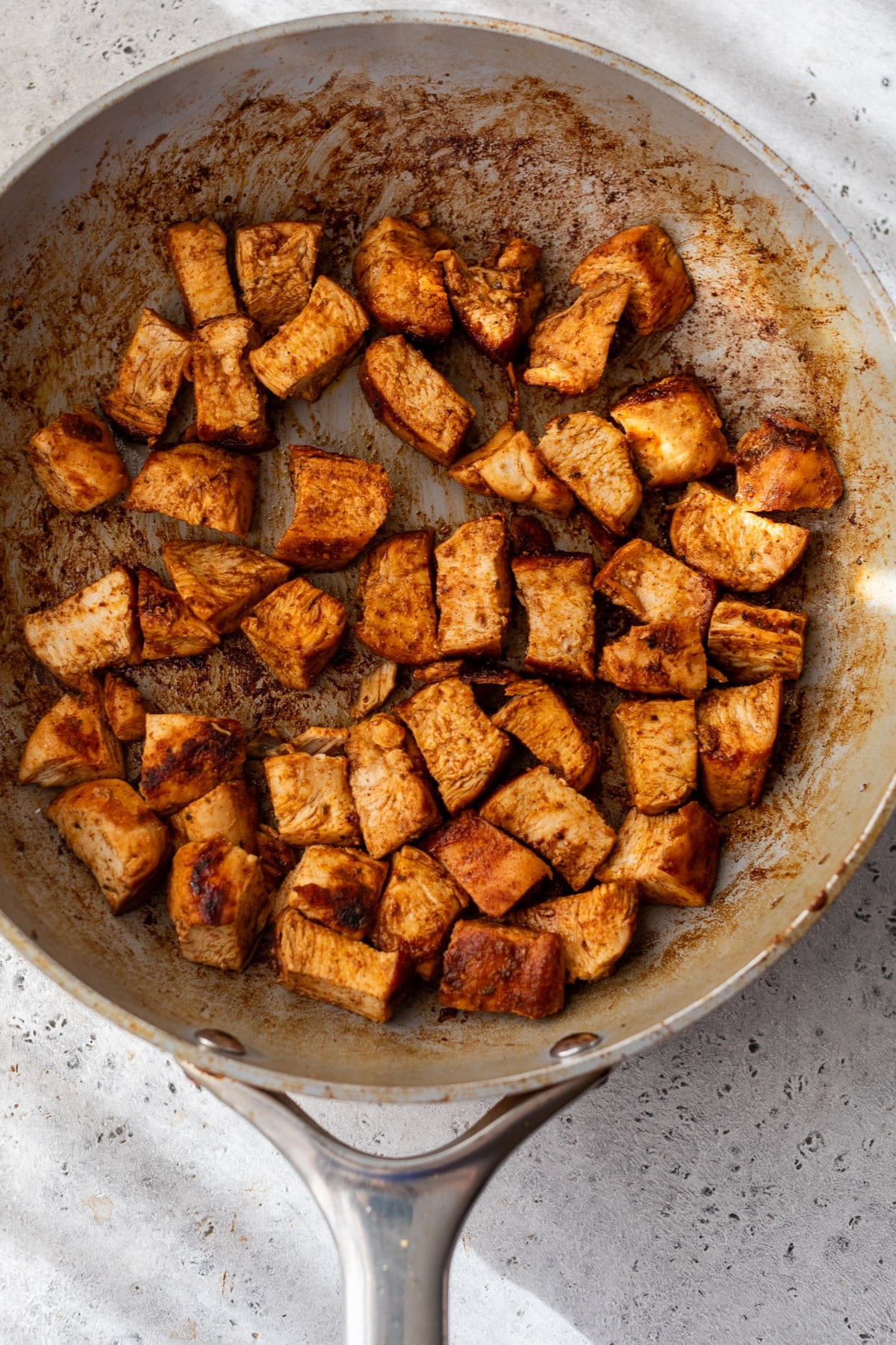 overhead view of taco-seasoned chicken pieces for a chicken taco salad in a skillet.