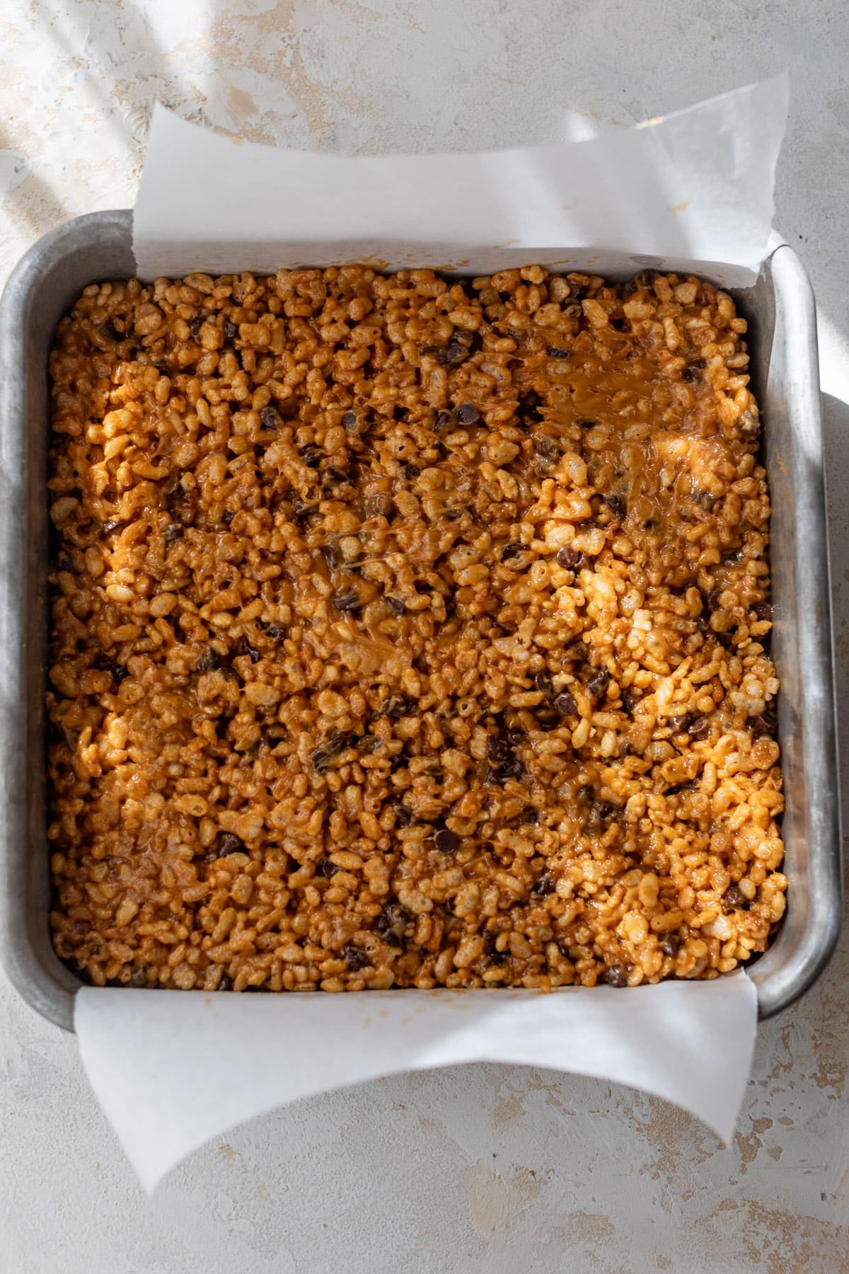 overhead view of Healthy Peanut Butter Rice Crispy Treats pressed into a square parchment-lined baking pan.