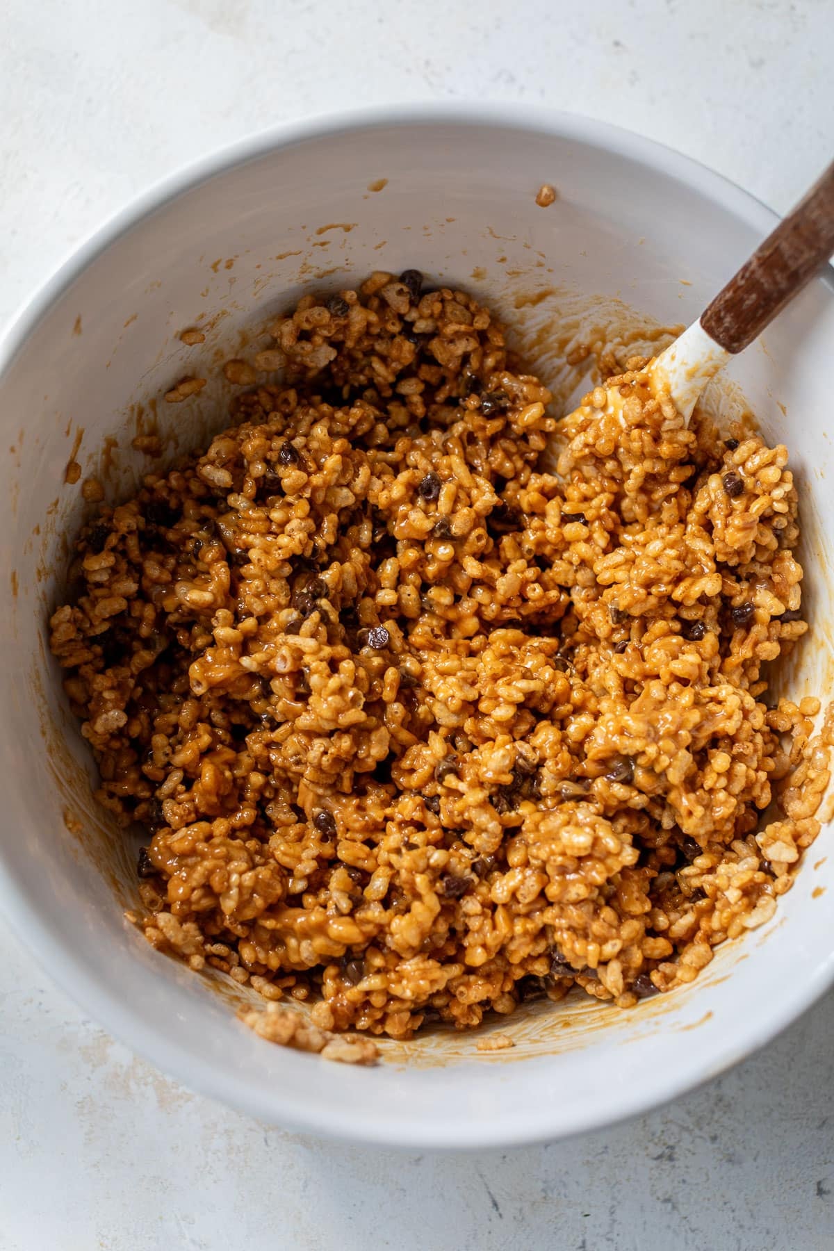 overhead view of the ingredients for Healthy Peanut Butter Rice Crispy Treats being mixed together with a spatula in a white bowl.