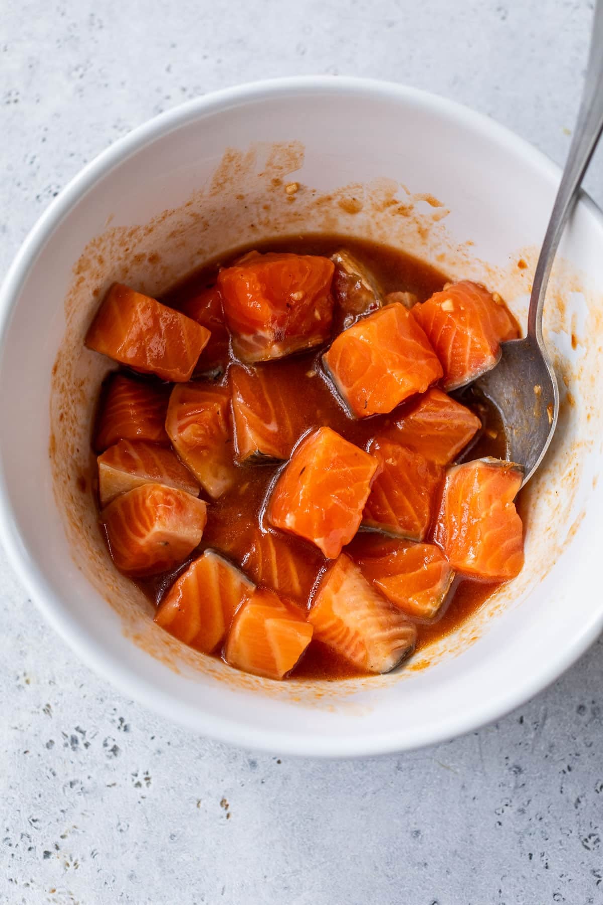 overhead view of a white bowl filled with raw salmon pieces and a brown marinade.