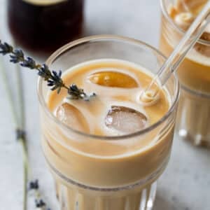 overhead view of two iced lavender dirty chai lattes in glasses with a glass straw and garnished with fresh lavender.