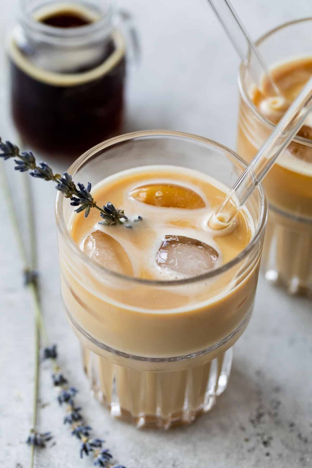 overhead view of two iced lavender dirty chai lattes in glasses with a glass straw and garnished with fresh lavender.