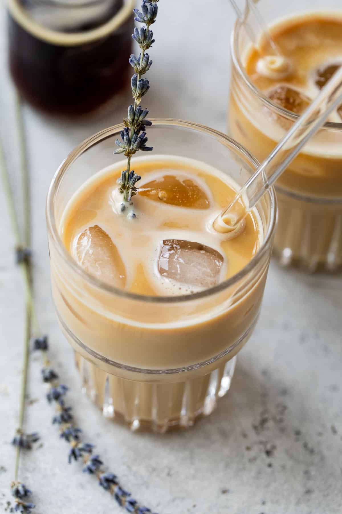 overhead view of two iced lavender dirty chai lattes in glasses with a glass straw and garnished with fresh lavender.