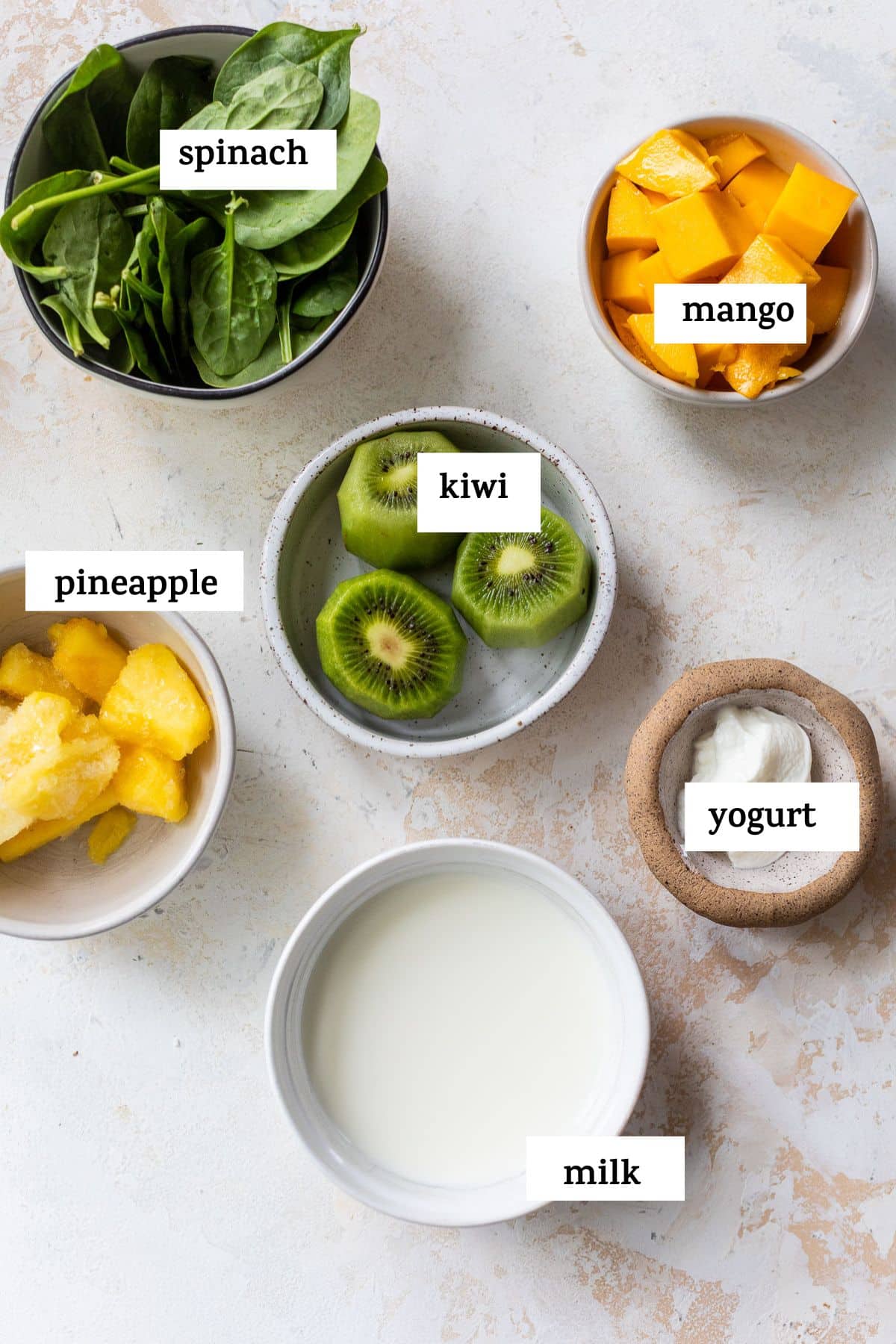 overhead view of the ingredients for a kiwi smoothie in individual bowls with labels.