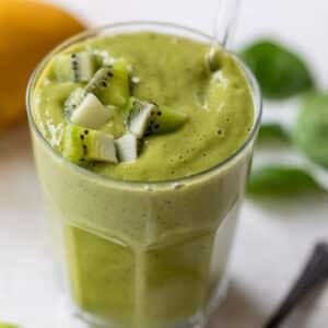 side view of a thick and green kiwi smoothie in a glass with chopped kiwi on top.