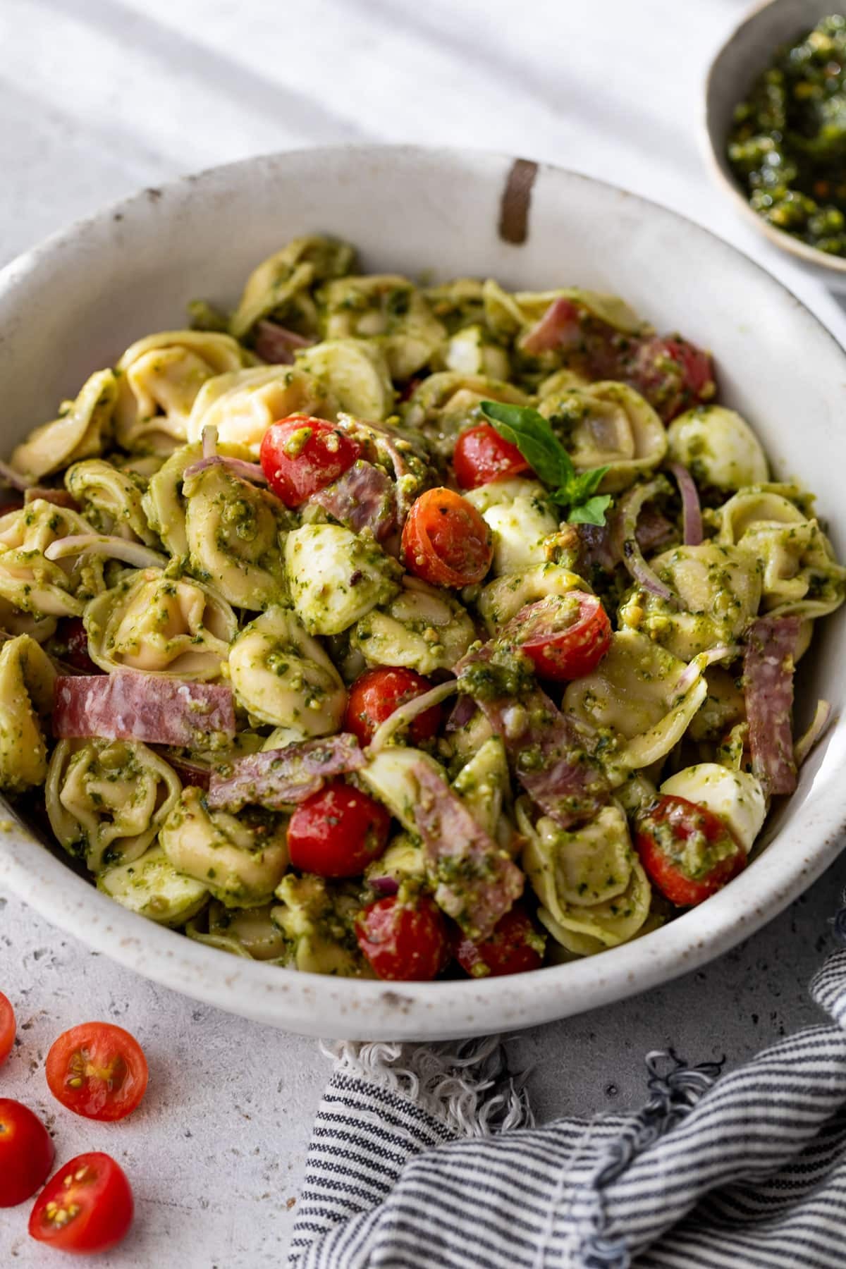 side view of a pesto-dressed tortellini pasta salad in a large white bowl.