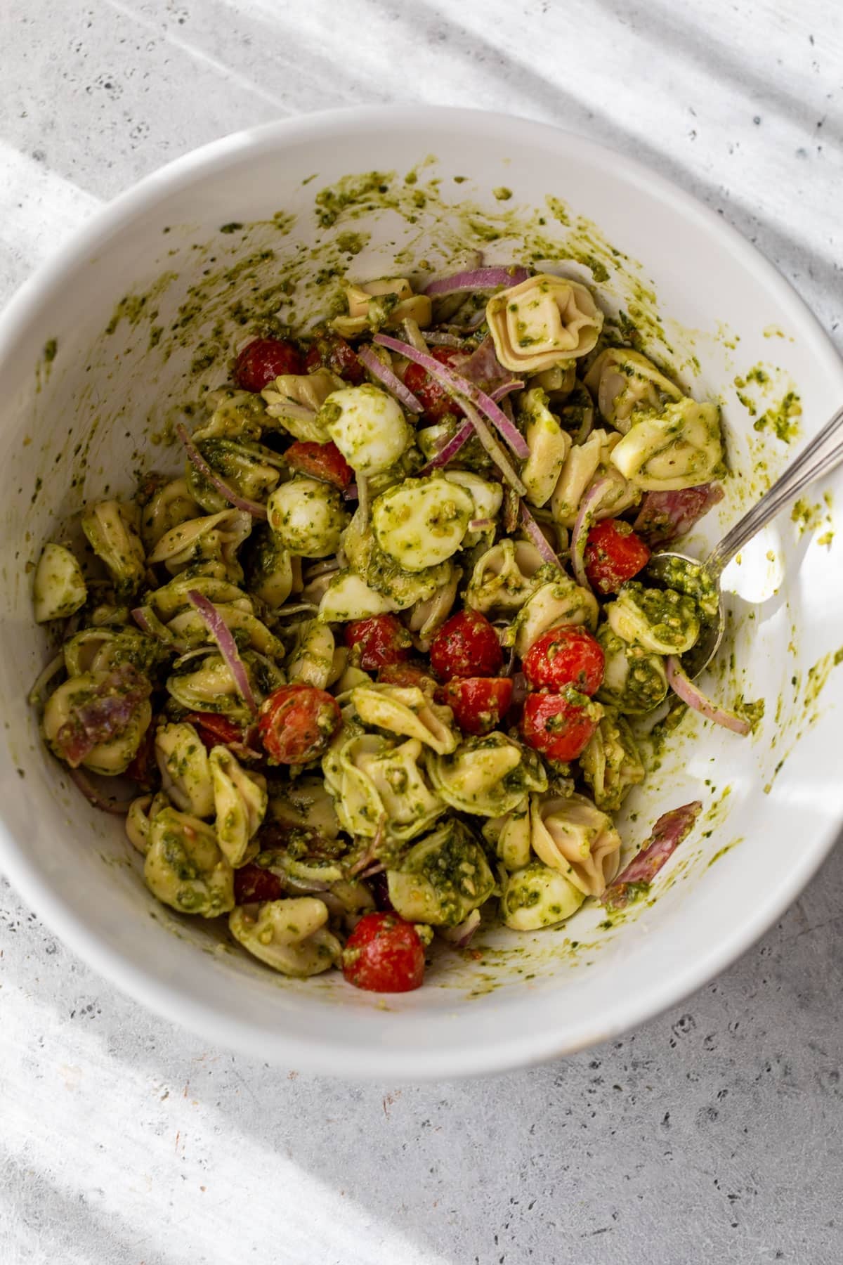 overhead view of the ingredients for a tortellini pasta salad being tossed together in a white bowl.