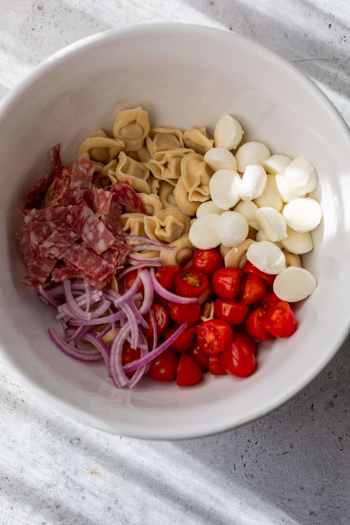 overhead view of the ingredients for a tortellini pasta salad together in a white bowl.