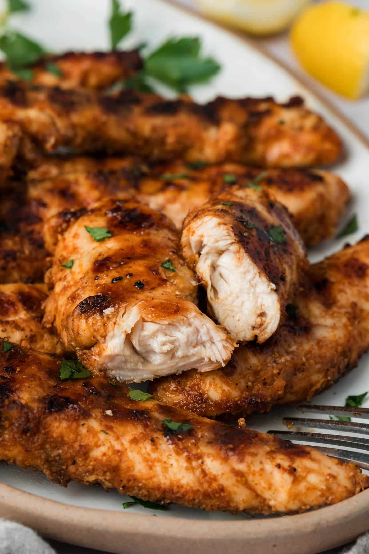 side view of a grilled chicken tender cut in half on top of a pile of other tenders.
