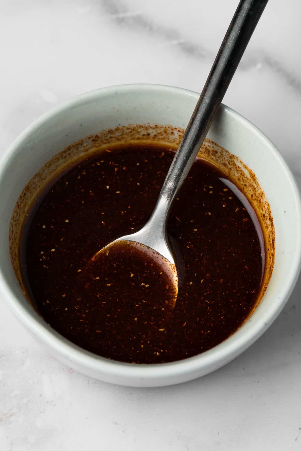 side view of a spoon and the chipotle marinade for grilled chicken tenders in a small bowl.