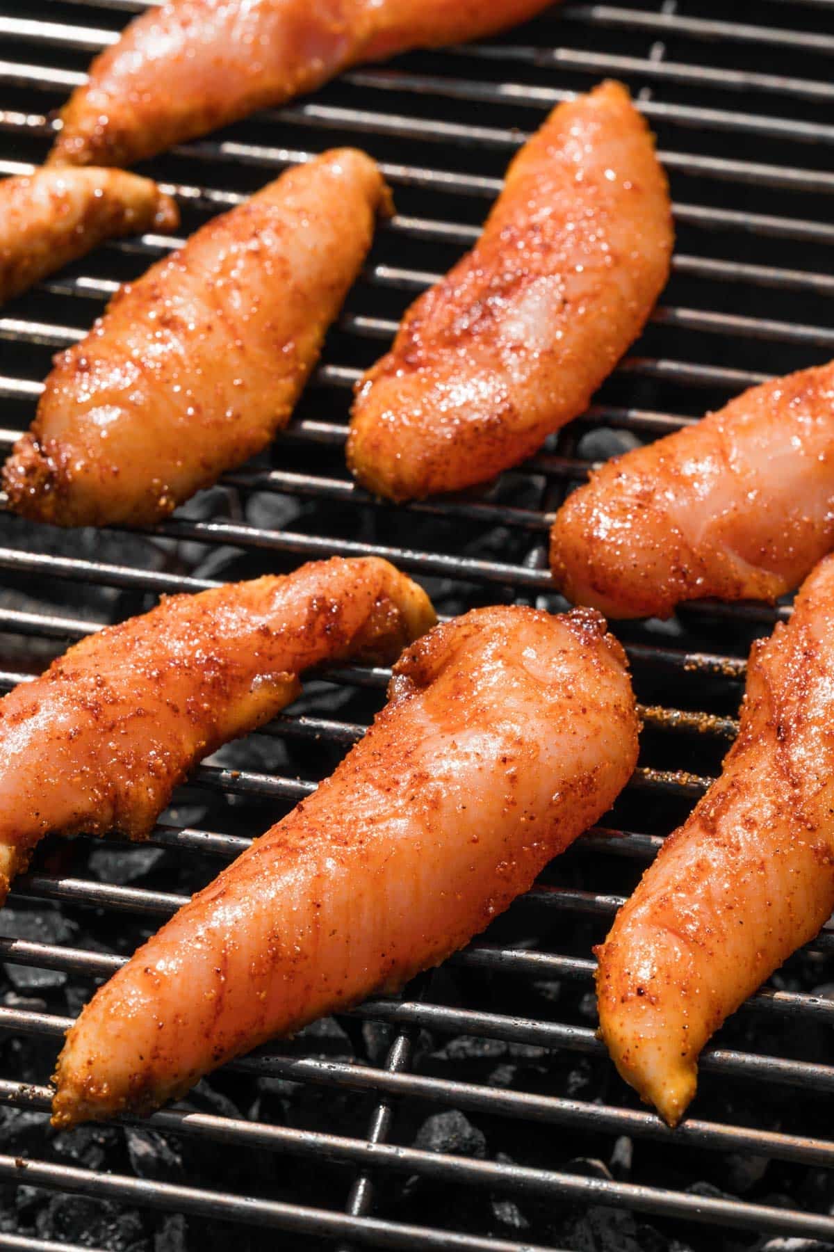 side view of raw marinated chicken tenders cooking on a grill.